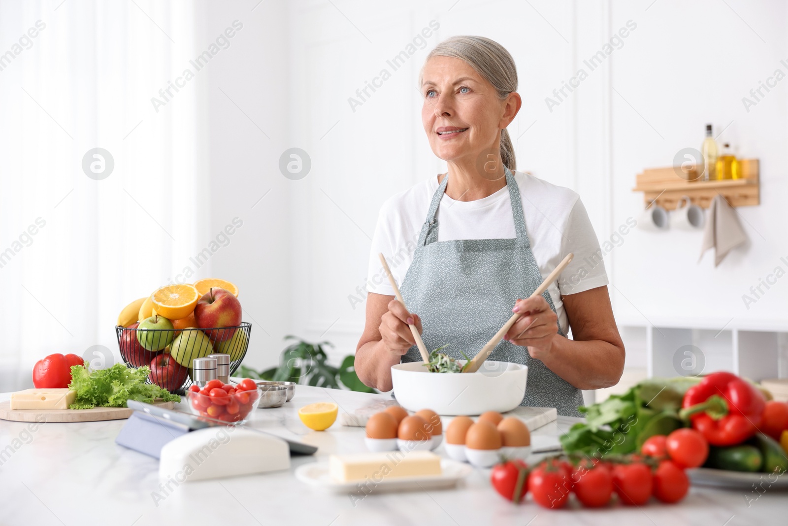 Senior woman cooking salad at white marble table in kitchen Photo of Senior woman cooking salad at white marble table in kitchen