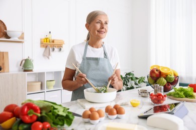 Photo of Senior woman cooking salad at white marble table in kitchen