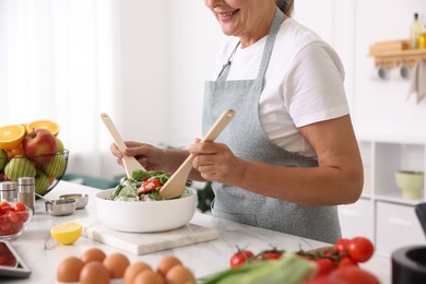Photo of Senior woman cooking salad at white marble table in kitchen, closeup