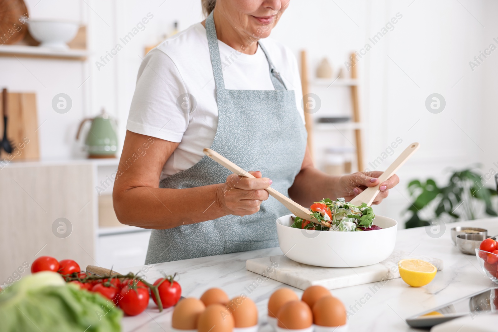 Senior woman cooking salad at white marble table in kitchen, closeup Photo of Senior woman cooking salad at white marble table in kitchen, closeup