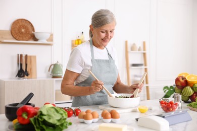 Photo of Senior woman cooking salad at white marble table in kitchen