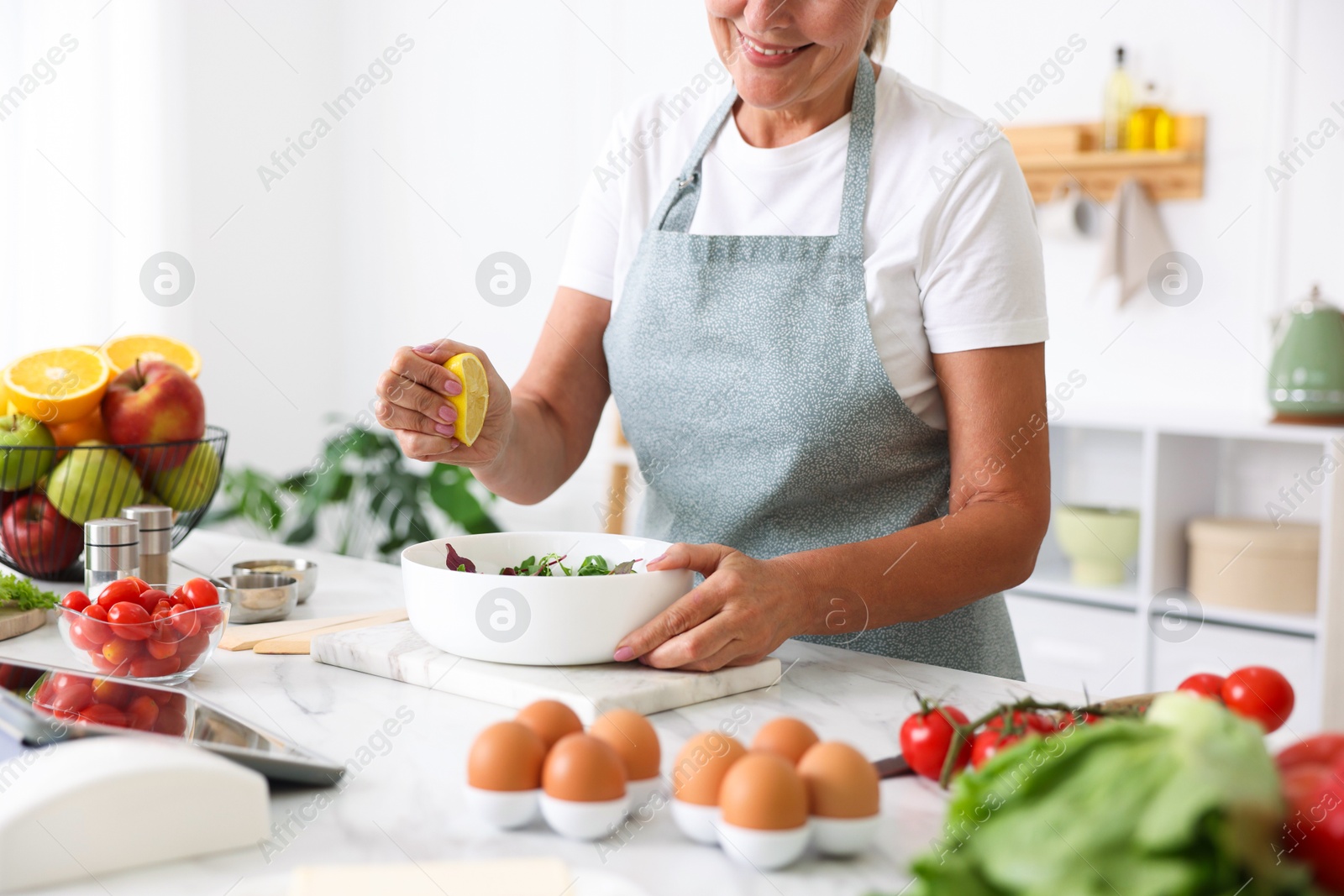 Photo of Senior woman cooking salad at white marble table in kitchen, closeup