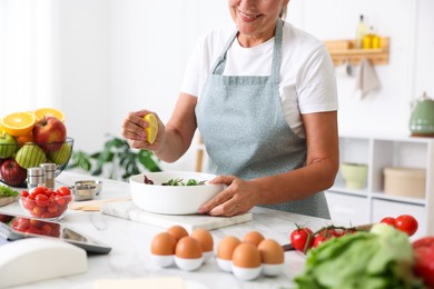 Photo of Senior woman cooking salad at white marble table in kitchen, closeup