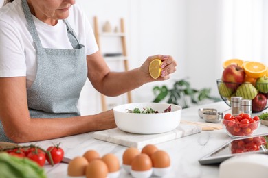 Photo of Senior woman cooking salad at white marble table in kitchen, closeup