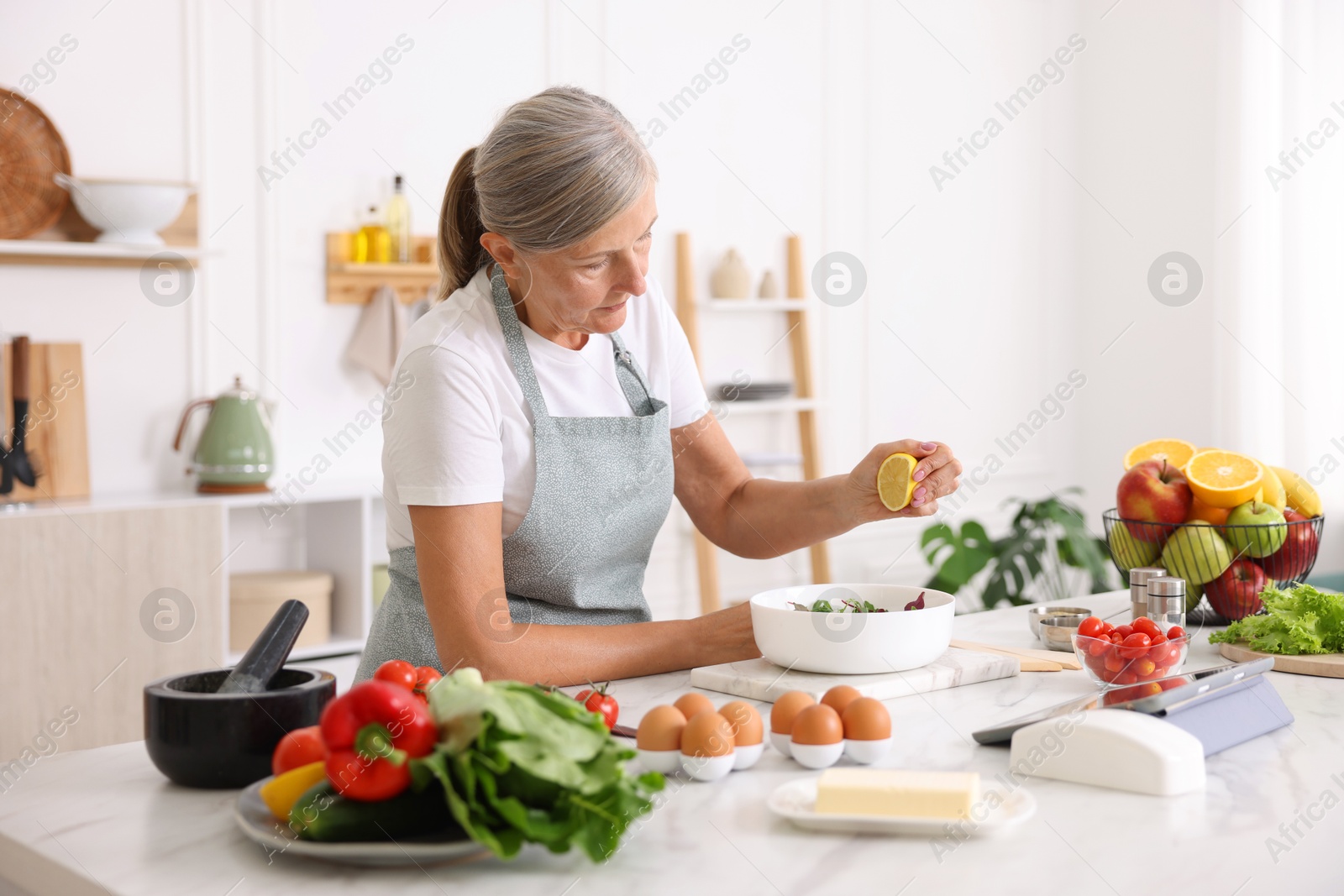 Senior woman cooking salad at white marble table in kitchen Photo of Senior woman cooking salad at white marble table in kitchen