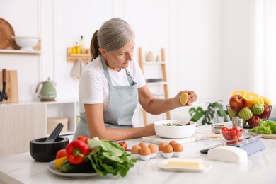 Photo of Senior woman cooking salad at white marble table in kitchen