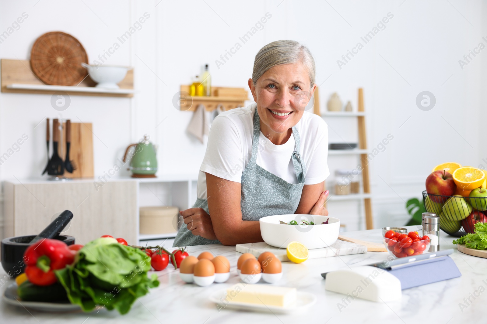 Senior woman cooking salad at white marble table in kitchen Photo of Senior woman cooking salad at white marble table in kitchen