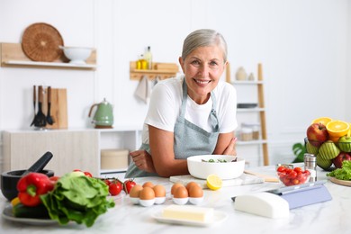 Photo of Senior woman cooking salad at white marble table in kitchen