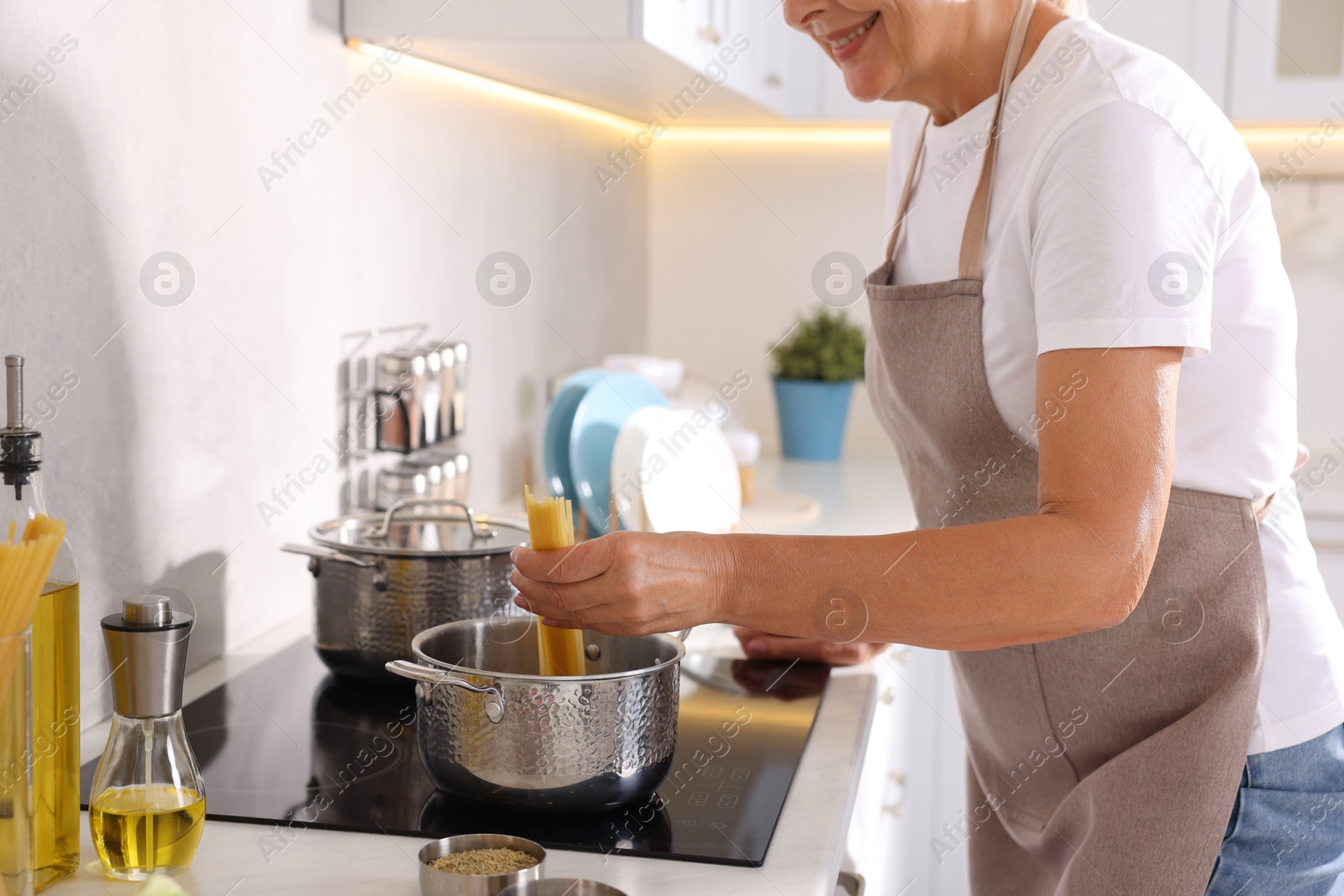 Senior woman cooking dish on cooktop in kitchen, closeup Photo of Senior woman cooking dish on cooktop in kitchen, closeup