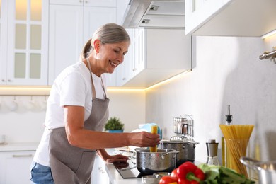 Photo of Senior woman cooking dish on cooktop in kitchen