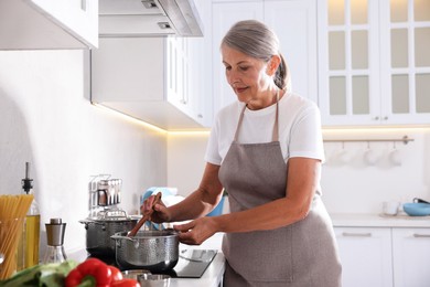 Photo of Senior woman cooking dish on cooktop in kitchen
