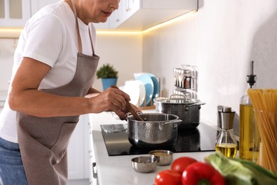 Photo of Senior woman cooking dish on cooktop in kitchen, closeup