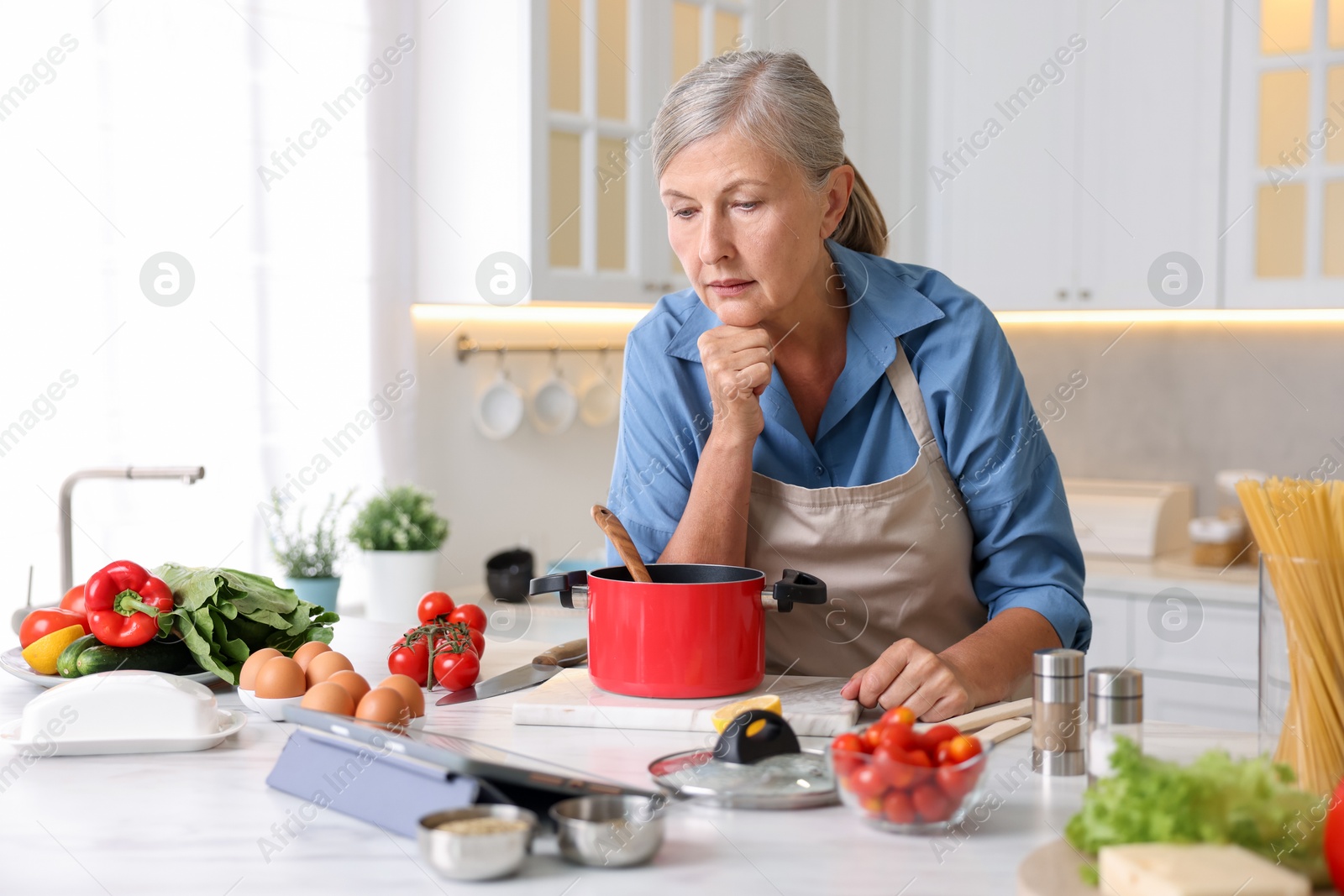 Senior woman using tablet while cooking at white marble table in kitchen Photo of Senior woman using tablet while cooking at white marble table in kitchen