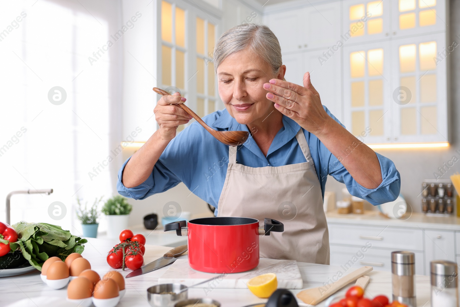 Senior woman cooking at white marble table in kitchen Photo of Senior woman cooking at white marble table in kitchen