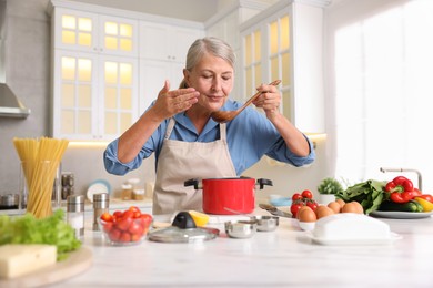 Photo of Senior woman cooking at white marble table in kitchen
