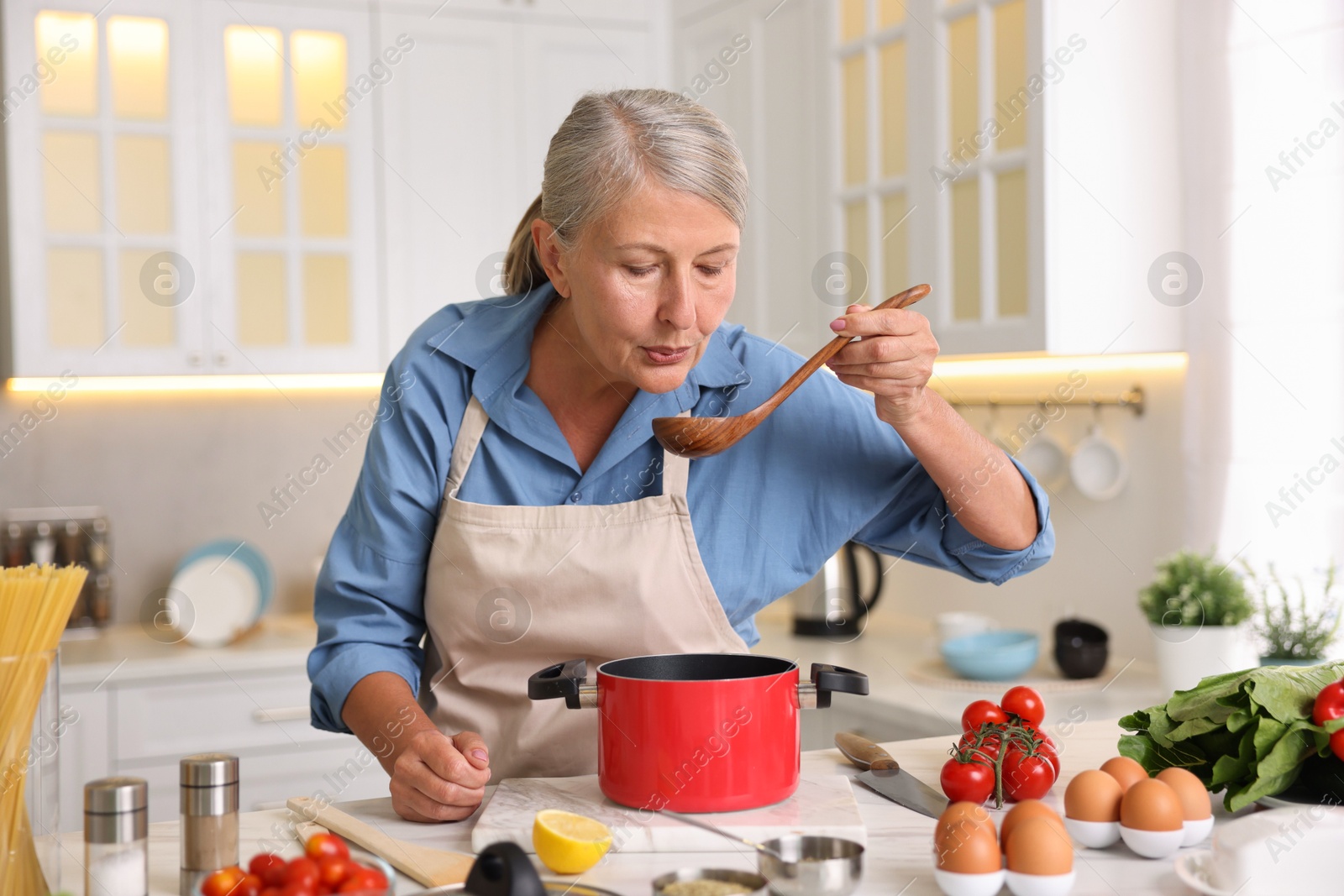 Senior woman cooking at white marble table in kitchen Photo of Senior woman cooking at white marble table in kitchen