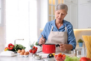 Photo of Senior woman cooking at white marble table in kitchen