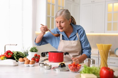 Photo of Senior woman cooking at white marble table in kitchen