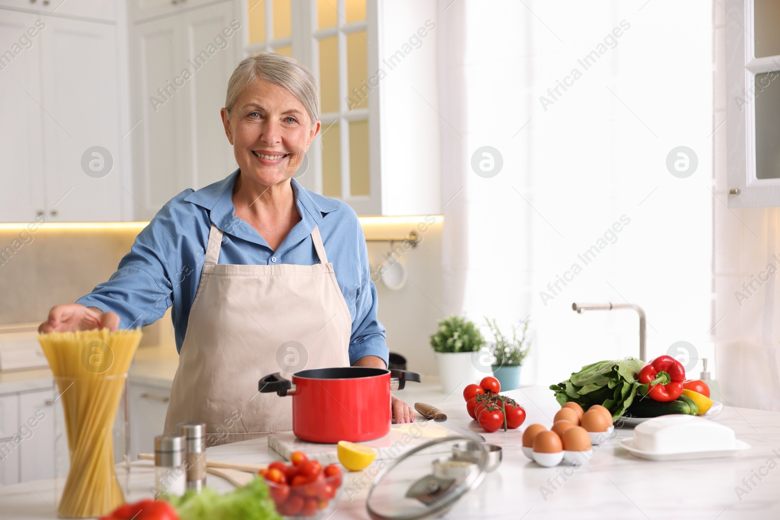 Senior woman cooking at white marble table in kitchen Photo of Senior woman cooking at white marble table in kitchen