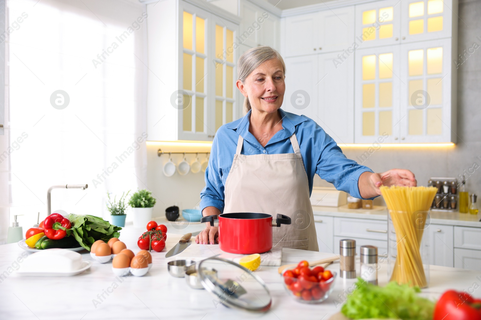 Senior woman cooking at white marble table in kitchen Photo of Senior woman cooking at white marble table in kitchen