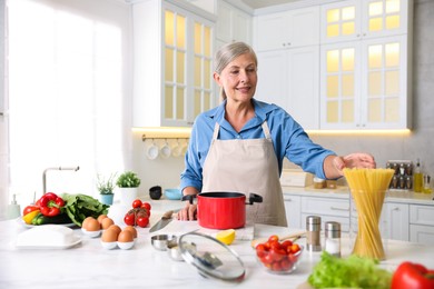 Photo of Senior woman cooking at white marble table in kitchen