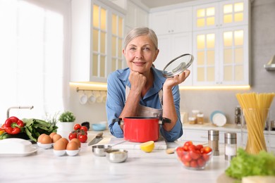 Photo of Senior woman cooking at white marble table in kitchen
