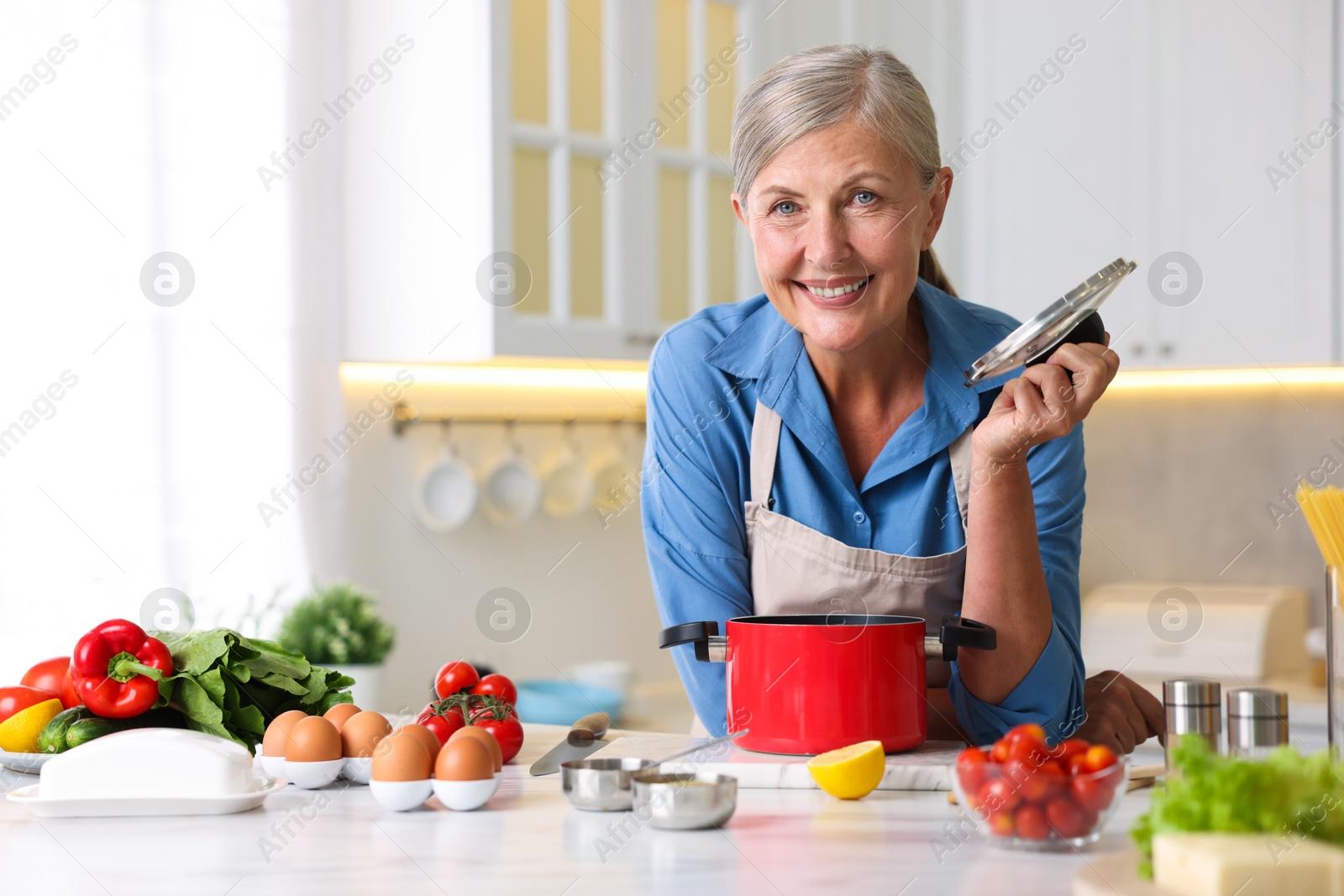 Senior woman cooking at white marble table in kitchen Photo of Senior woman cooking at white marble table in kitchen