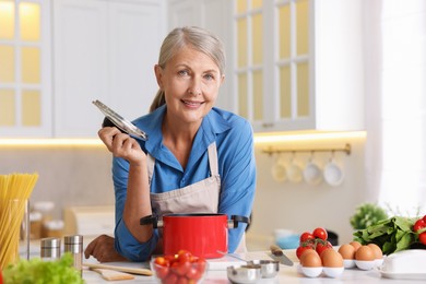 Photo of Senior woman cooking salad at table in kitchen