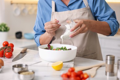 Photo of Senior woman cooking salad at white marble table in kitchen, closeup