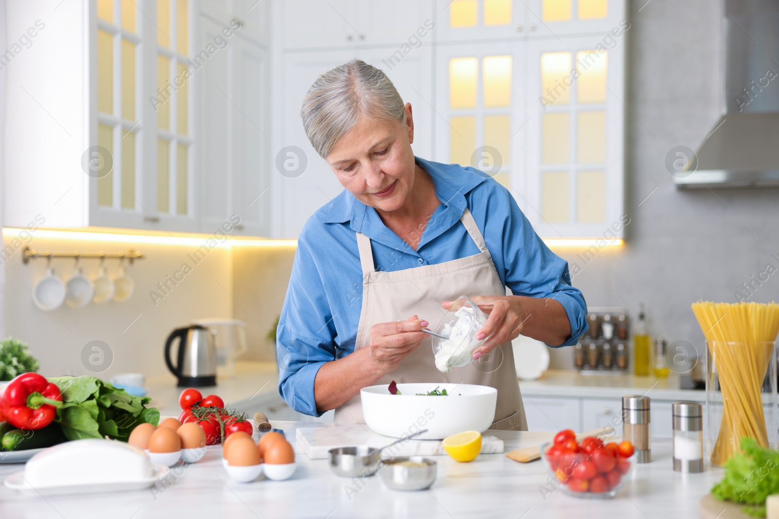 Senior woman cooking salad at white marble table in kitchen Photo of Senior woman cooking salad at white marble table in kitchen