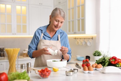 Photo of Senior woman cooking salad at white marble table in kitchen