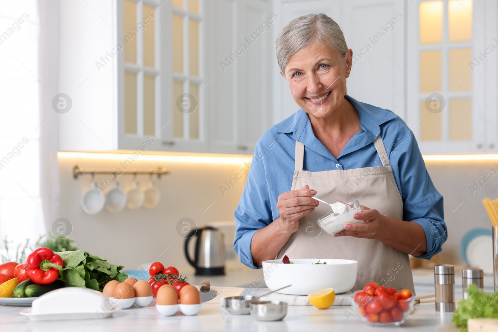 Senior woman cooking salad at white marble table in kitchen Photo of Senior woman cooking salad at white marble table in kitchen