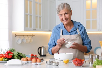Photo of Senior woman cooking salad at white marble table in kitchen