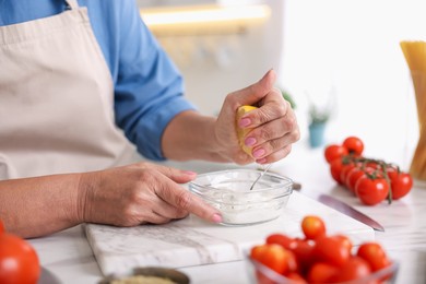 Photo of Senior woman cooking at white marble table in kitchen, closeup