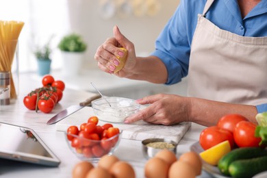 Photo of Senior woman cooking at white marble table in kitchen, closeup