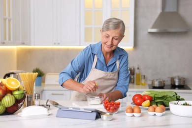 Photo of Senior woman cooking at white marble table in kitchen