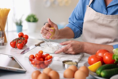 Photo of Senior woman cooking at white marble table in kitchen, closeup