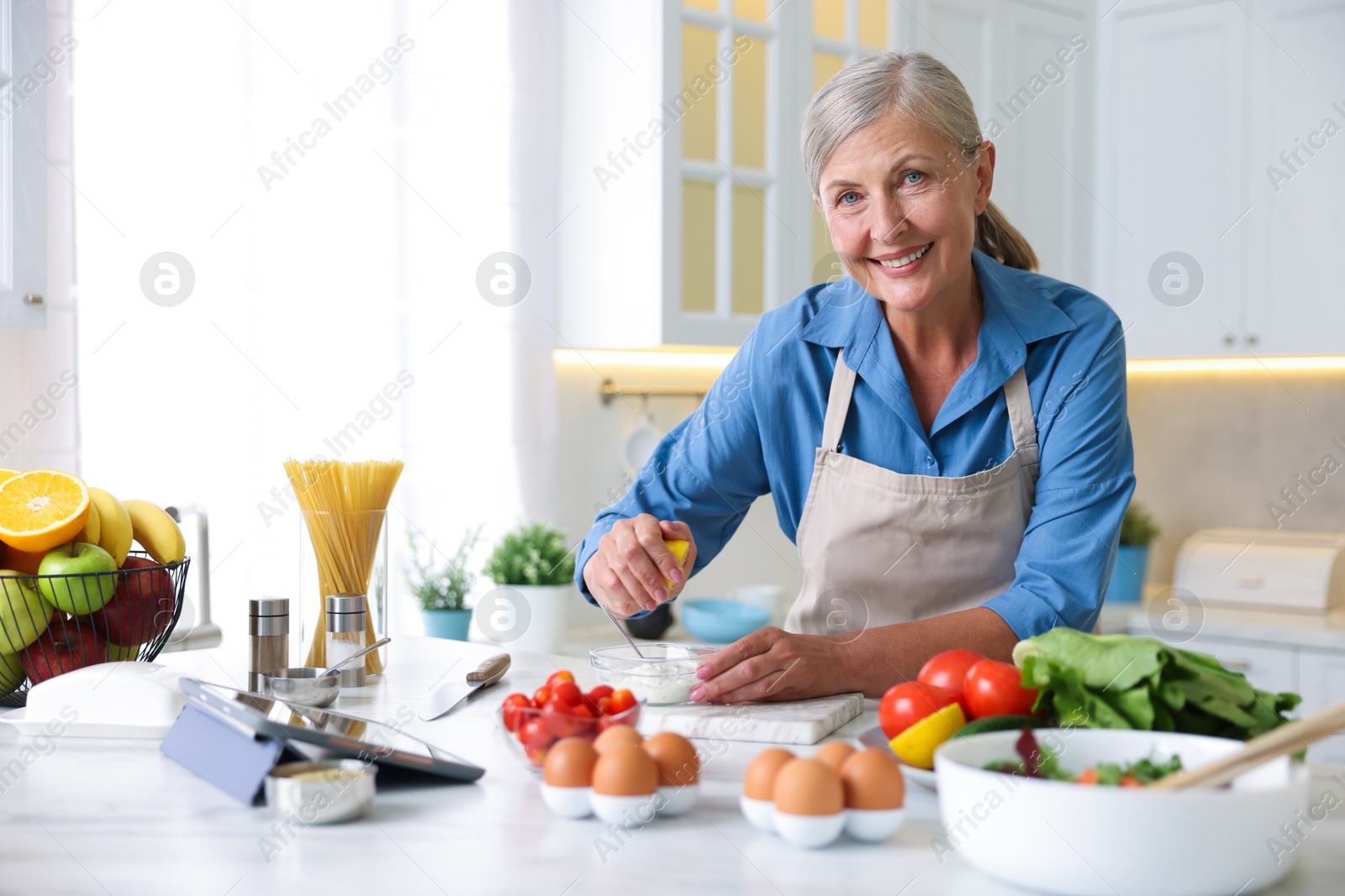 Senior woman cooking at white marble table in kitchen Photo of Senior woman cooking at white marble table in kitchen