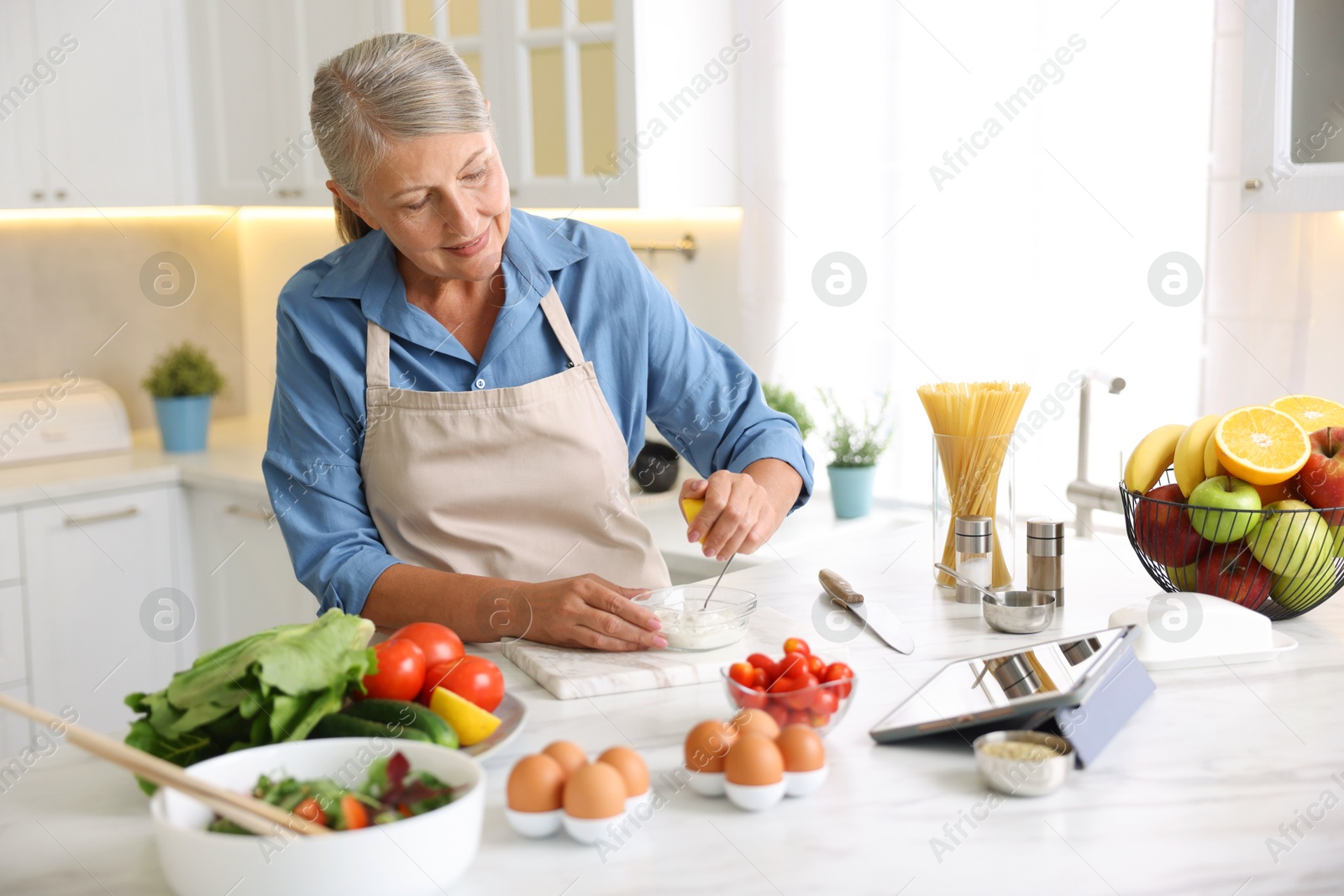 Senior woman cooking at white marble table in kitchen Photo of Senior woman cooking at white marble table in kitchen