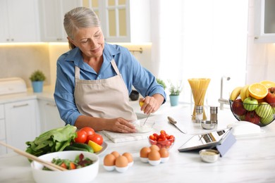 Photo of Senior woman cooking at white marble table in kitchen