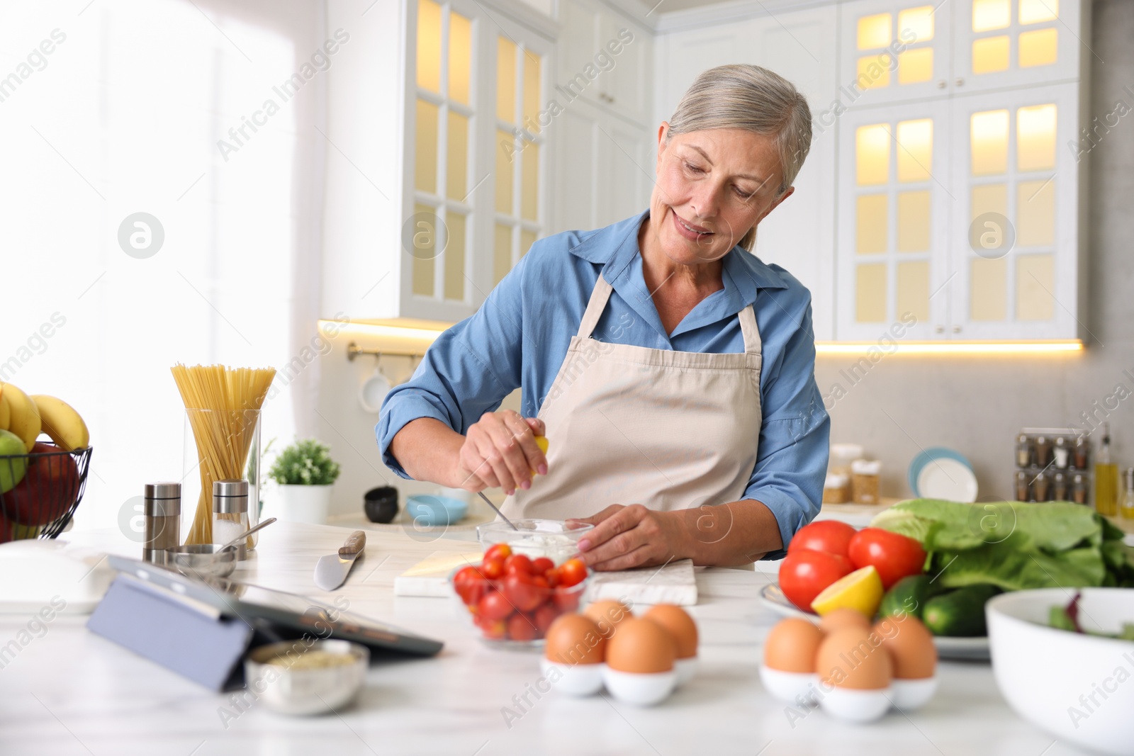 Senior woman cooking at white marble table in kitchen Photo of Senior woman cooking at white marble table in kitchen