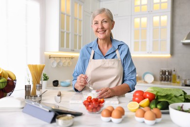 Photo of Senior woman cooking at white marble table in kitchen