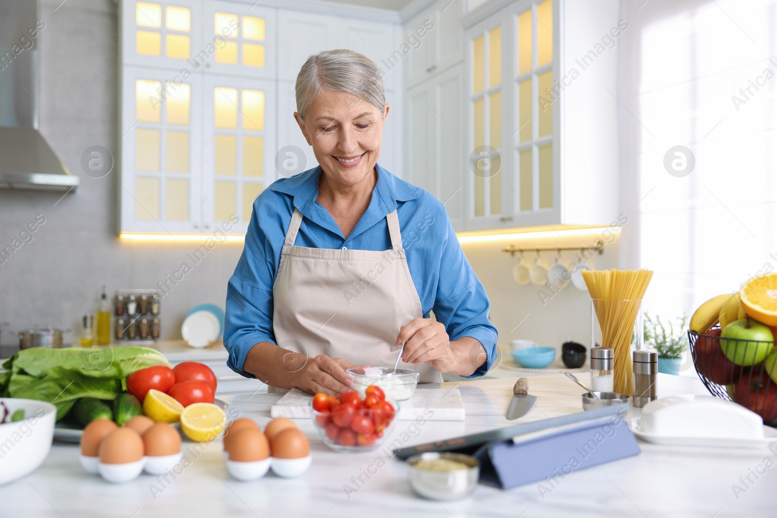 Senior woman cooking at white marble table in kitchen Photo of Senior woman cooking at white marble table in kitchen