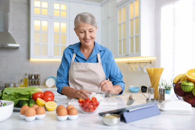 Photo of Senior woman cooking at white marble table in kitchen