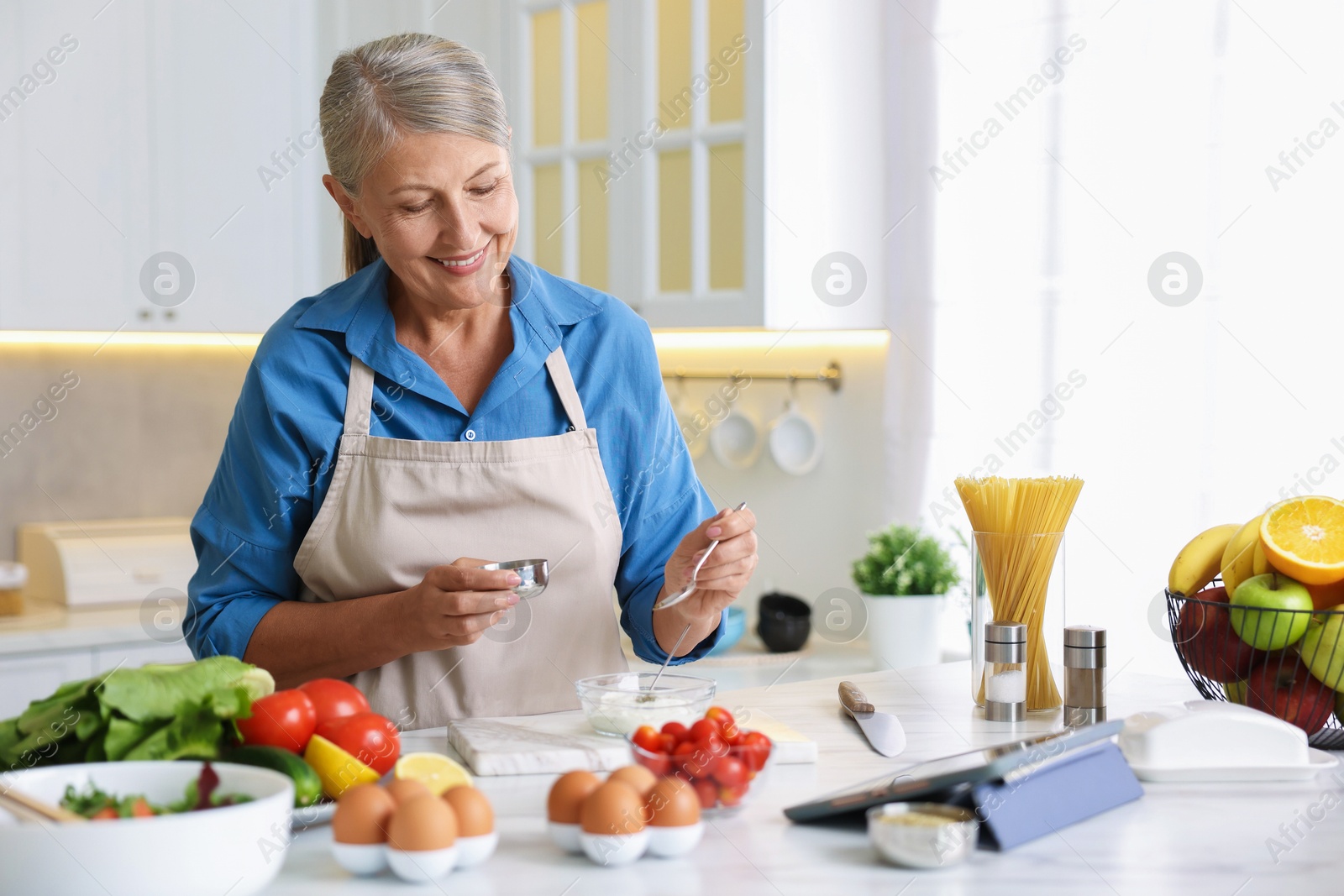 Senior woman cooking at white marble table in kitchen Photo of Senior woman cooking at white marble table in kitchen