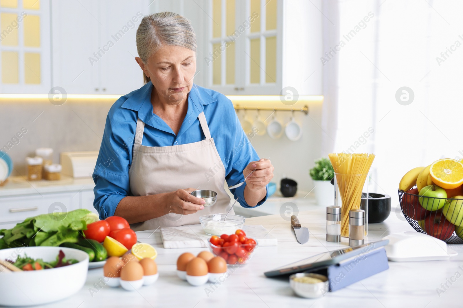 Senior woman cooking at white marble table in kitchen Photo of Senior woman cooking at white marble table in kitchen