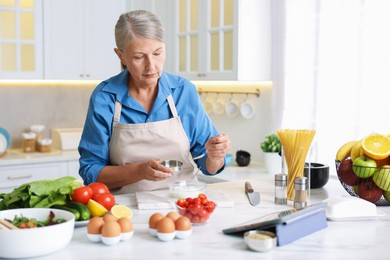 Photo of Senior woman cooking at white marble table in kitchen