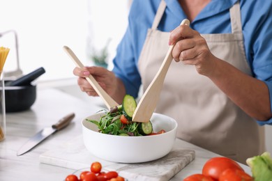 Photo of Senior woman cooking salad at white marble table in kitchen, closeup