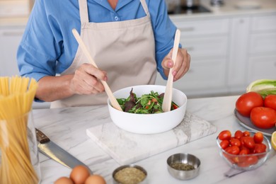 Photo of Senior woman cooking salad at white marble table in kitchen, closeup