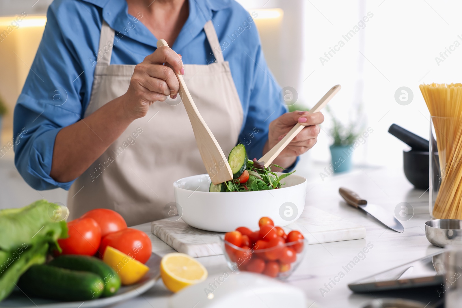Senior woman cooking salad at white marble table in kitchen, closeup Photo of Senior woman cooking salad at white marble table in kitchen, closeup